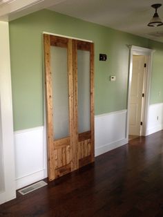 an empty room with green walls and wooden floors, two doors are open to the hallway