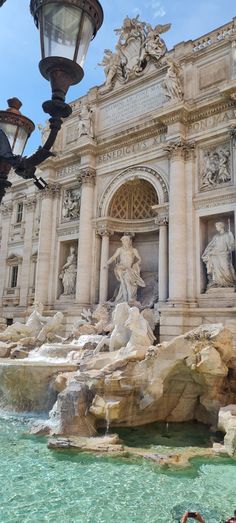 a fountain in front of a large building with statues on it's sides and a lamp post