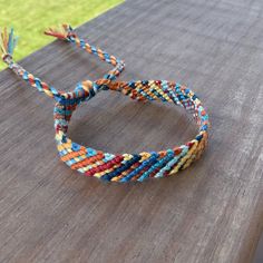 two colorful bracelets sitting on top of a wooden table next to a green field