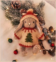 a knitted teddy bear wearing a red and white dress next to pine cones and christmas decorations