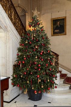 a christmas tree with red and gold ornaments is in the corner of a room next to stairs