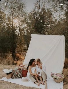 a woman sitting on top of a blanket next to a man holding a baby in front of a tent