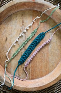 three crocheted bracelets are on a wooden platter with yarn in it