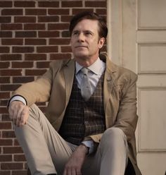 a man sitting on the ground in front of a brick wall wearing a suit and tie