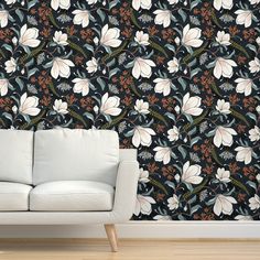 a white couch sitting in front of a black wallpaper with flowers and leaves on it