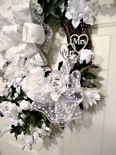 a wreath with white flowers and ribbons hanging on the front door to say mr and mrs