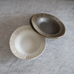 two white plates sitting on top of a cement floor next to each other, with one empty plate in the middle