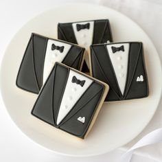 four decorated cookies in the shape of tuxedos are on a plate with white cloth