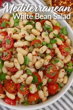 a white bowl filled with pasta and tomatoes on top of a striped table cloth next to a wooden spoon