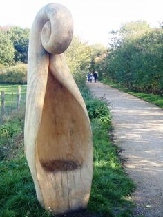 a large wooden sculpture sitting on top of a lush green field next to a road