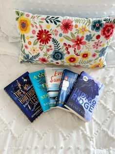 five books laying on top of a bed next to a pillow with an embroidered cover