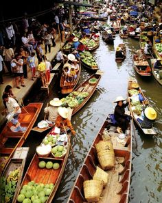 many small boats filled with fruits and vegetables floating on top of a river next to buildings