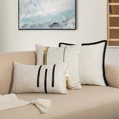 three pillows on a couch in front of a painting hanging above the couch is a throw pillow with black and white stripes