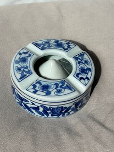 a blue and white porcelain container on a gray cloth with a metal lid in the shape of a flower