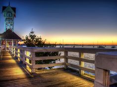 a clock tower sitting on the side of a wooden pier next to water at sunset