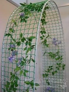 two green plants growing out of the side of a metal wire planter with blue flowers on it