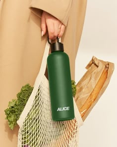 a person holding a green water bottle in their left hand and a grocery bag on the other