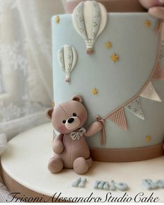 a teddy bear sitting on top of a blue and white cake with hot air balloons