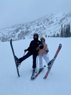 two people standing on top of a snow covered slope with skis and poles in their hands