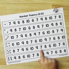 a hand is pointing at a number fluency sheet on a table with dices