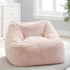 a pink bean bag chair sitting on top of a white rug next to a window