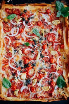 a square pizza with tomatoes, onions and basil