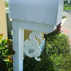 a white mailbox sitting on the side of a road next to bushes and trees