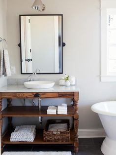 a white bath tub sitting next to a bathroom sink under a large mirror above a wooden vanity