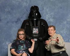 two people sitting on a couch in front of a darth vader statue with their hands out