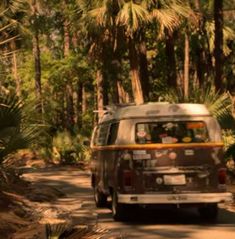 an old van driving down a dirt road in the woods with palm trees behind it