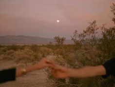 two people reaching out their hands to touch each other in the desert at night time