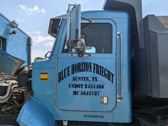 an old blue truck parked in front of a building with the door open and it's hood up