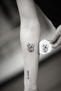 a person with a tattoo on their arm holding a small teddy bear in front of them