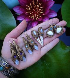 a person's hand holding seven pairs of earrings and a flower in the background