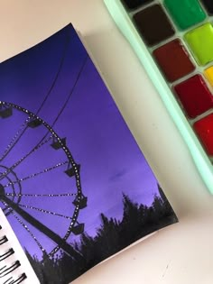 a painting of a ferris wheel with watercolors next to it on a table