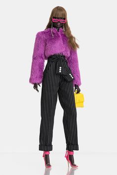 a woman in purple fur coat and black pinstripe pants holding a yellow purse