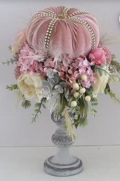 a pink velvet pumpkin sitting on top of a silver vase filled with flowers and feathers