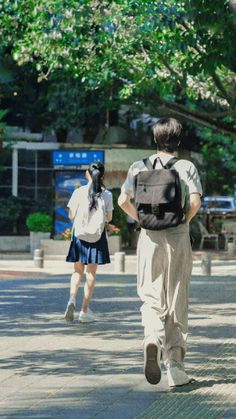 two people are walking down the street with backpacks on their back and one is carrying a book bag