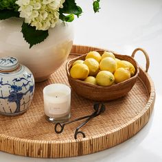 a bowl of lemons on a tray next to a vase with flowers in it