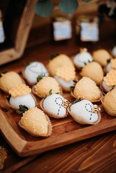 small cookies with white frosting are arranged on a wooden platter, along with honeycombs and strawberries