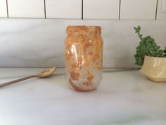 a glass jar sitting on top of a counter next to a wooden spoon and potted plant