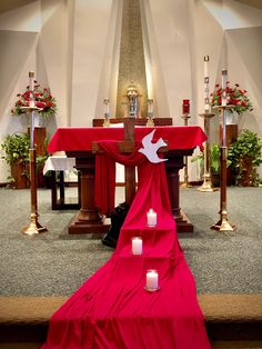 a red cloth draped over the alter at a church with candles in front of it