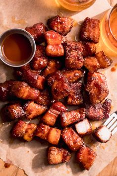 chicken wings with sauce and two cups of beer next to it on a piece of parchment paper