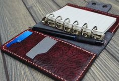 a notebook and pen sitting on top of a red leather case next to each other