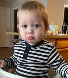 a toddler sitting in a high chair making a funny face