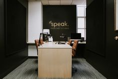 an office with black walls and wooden desks in the center, along with a speaker studio logo on the wall