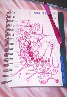 a spiral notebook with pink ink on it next to a pen and paper clipping