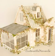 a doll house with flowers growing on the roof and windows, in front of a white wall