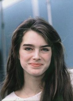 a woman with long brown hair smiling at the camera and wearing a white sweater over her shoulders