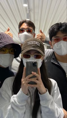 three people wearing face masks and holding up their cell phones to take a selfie